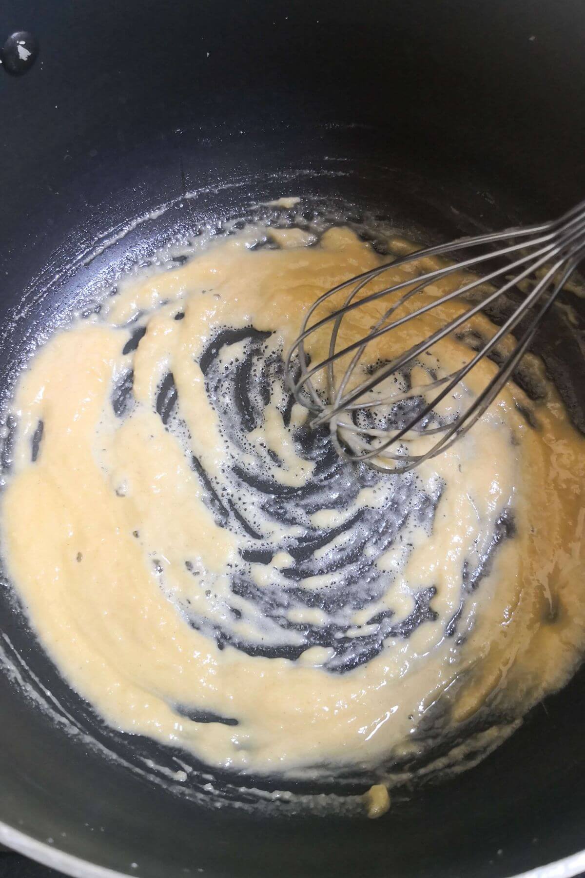 A roux being whisked in a large black pot.