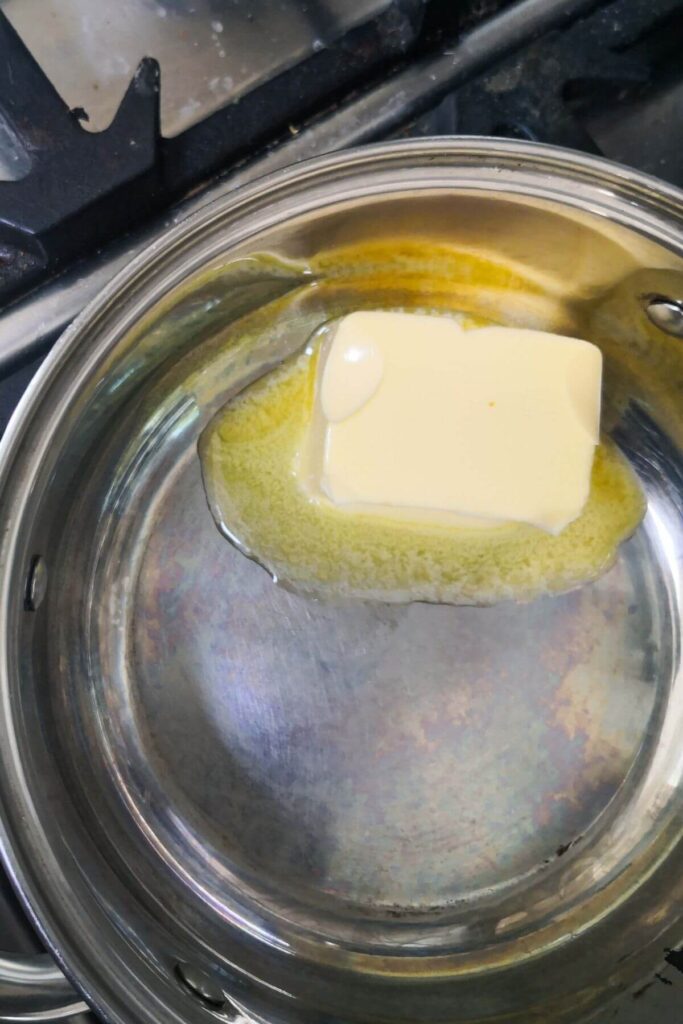 Butter starting to melt in a small silver pan on the stove top.