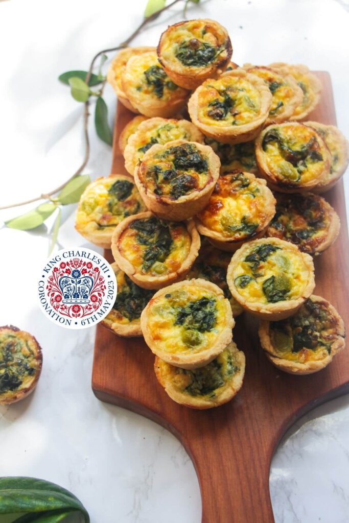 Mini coronation quiches piled up on a small wooden board.