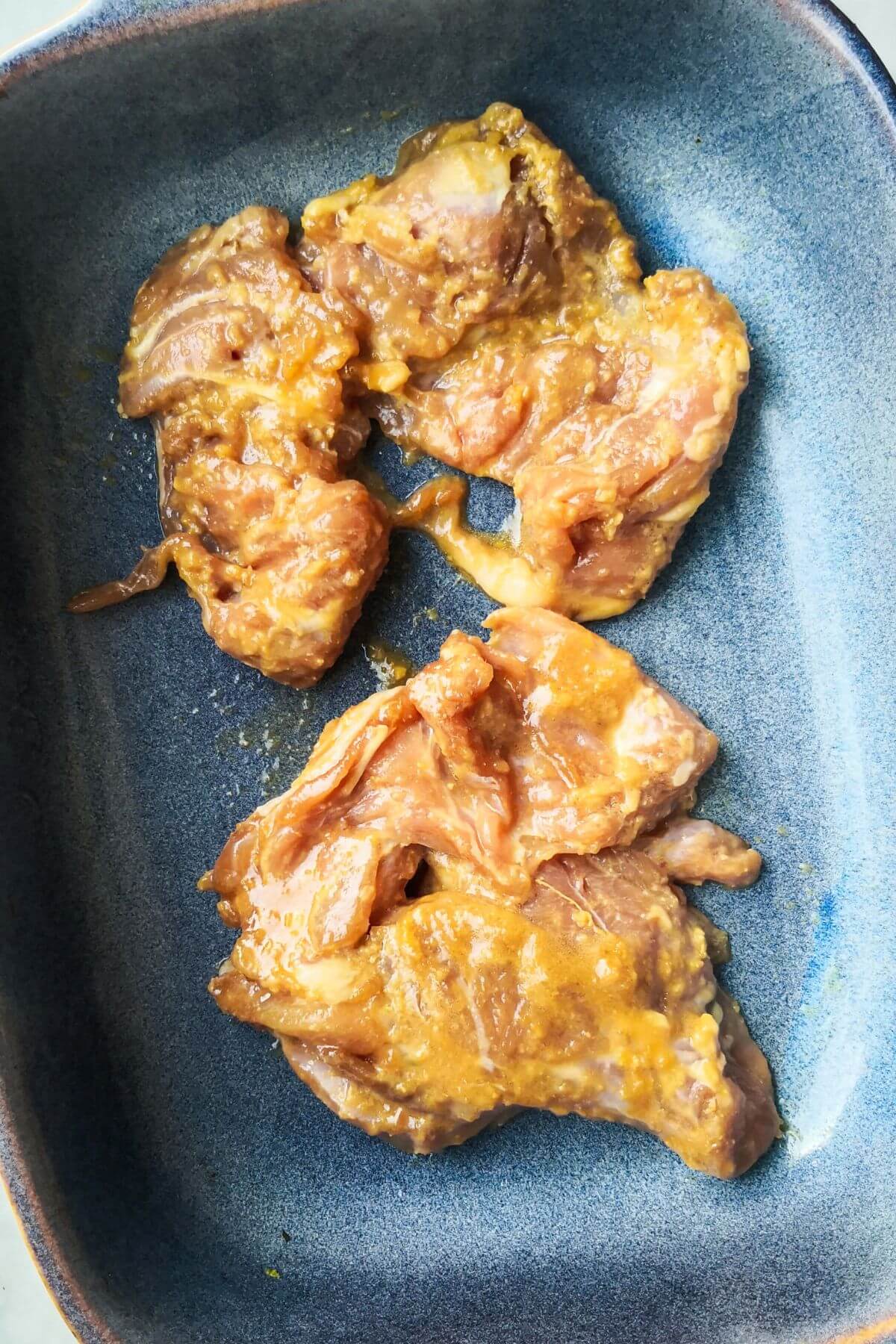 Raw miso marinated chicken thighs in a small blue oven dish.