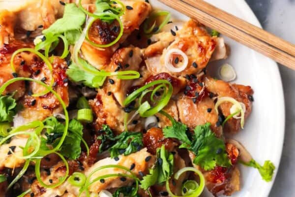 Miso grilled chicken sliced on a white plate, topped with coriander, spring onion and sesame seeds with a pot of chilli jam in the background.