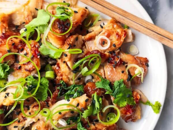 Miso grilled chicken sliced on a white plate, topped with coriander, spring onion and sesame seeds with a pot of chilli jam in the background.