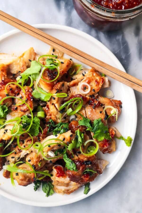 Miso grilled chicken sliced on a white plate, topped with coriander, spring onion and sesame seeds with a pot of chilli jam in the background.