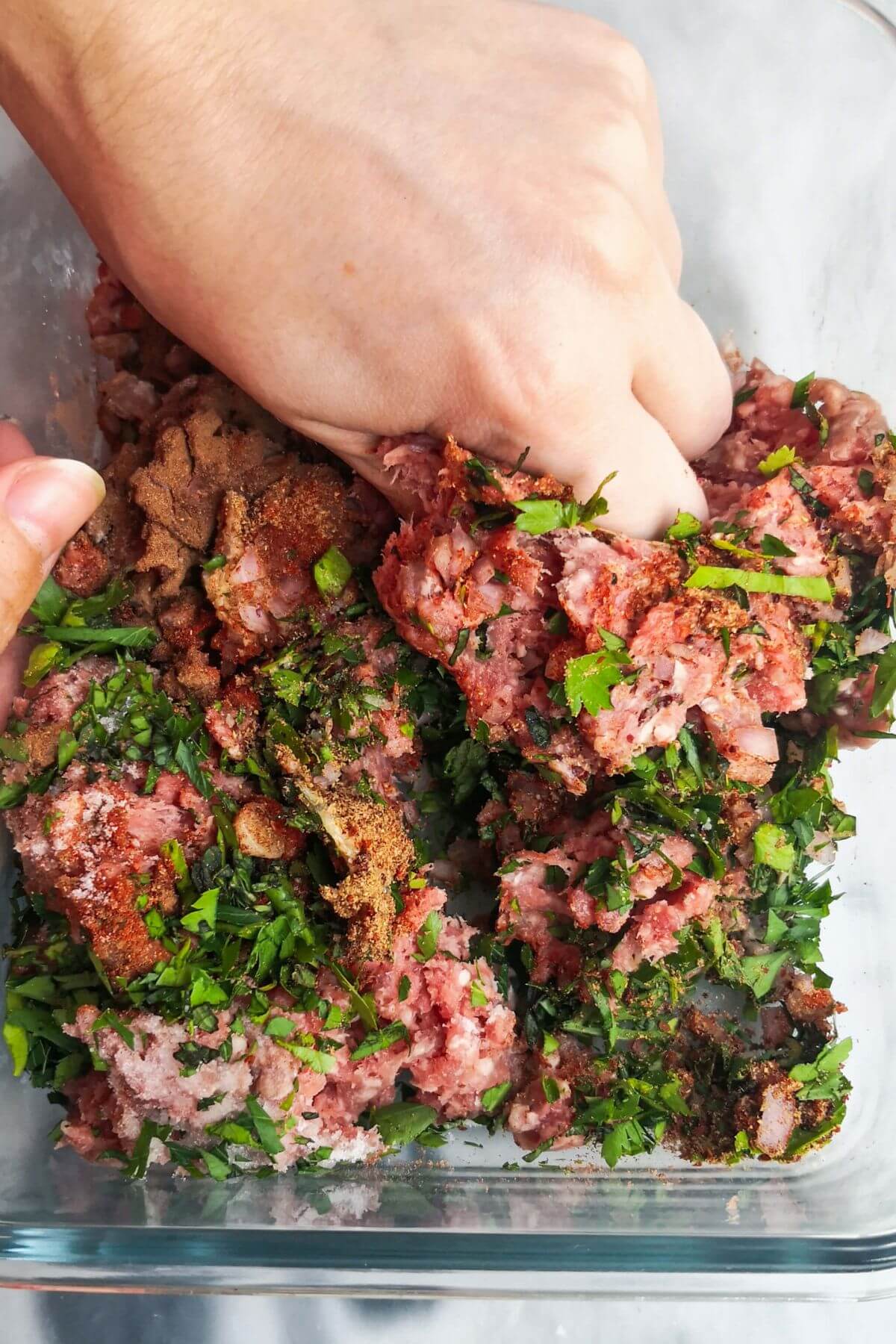 A hand scrunching together the lamb kofta ingredients in a glass container.