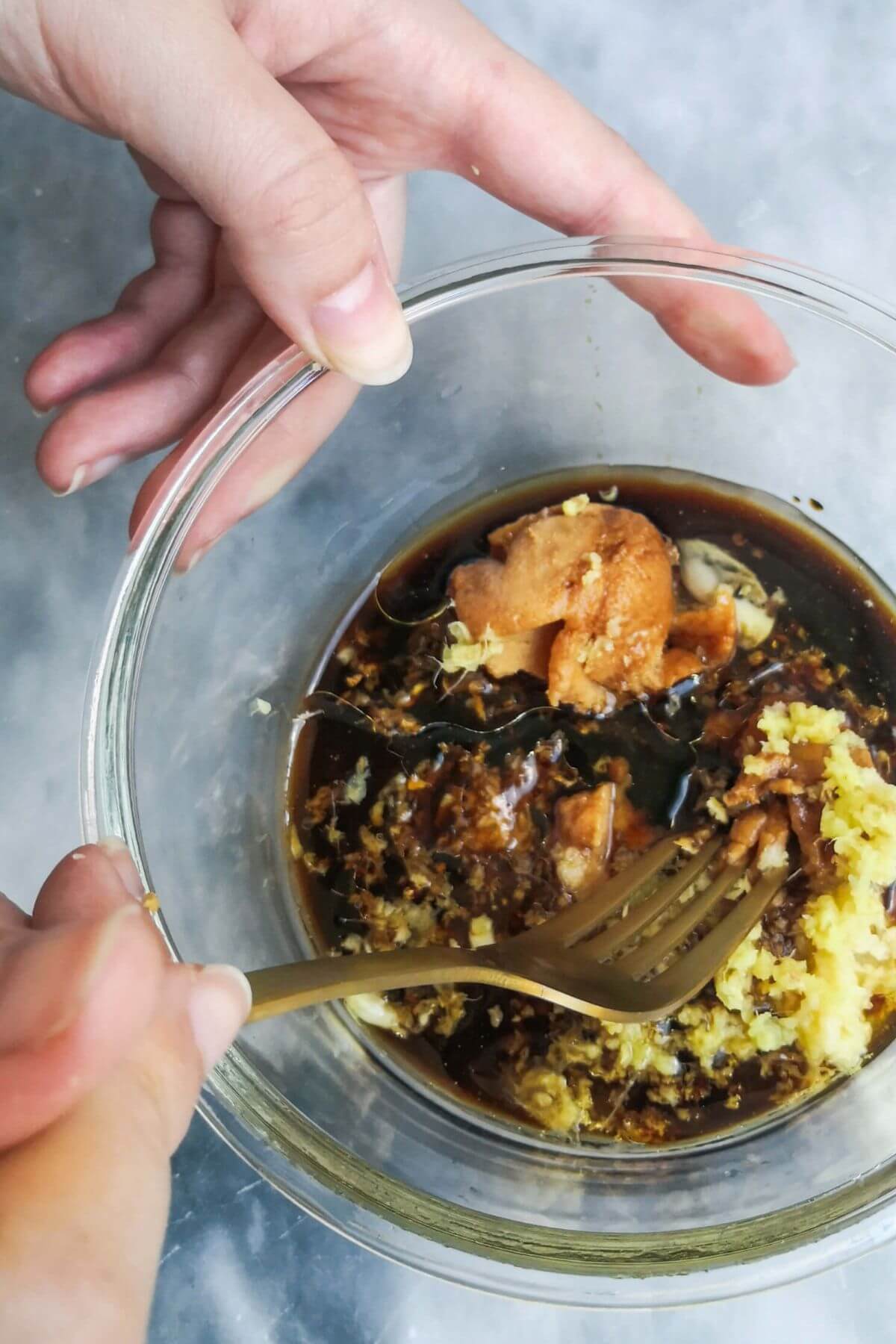 Mixing miso marinade ingredients in a small glass bowl with a gold fork.