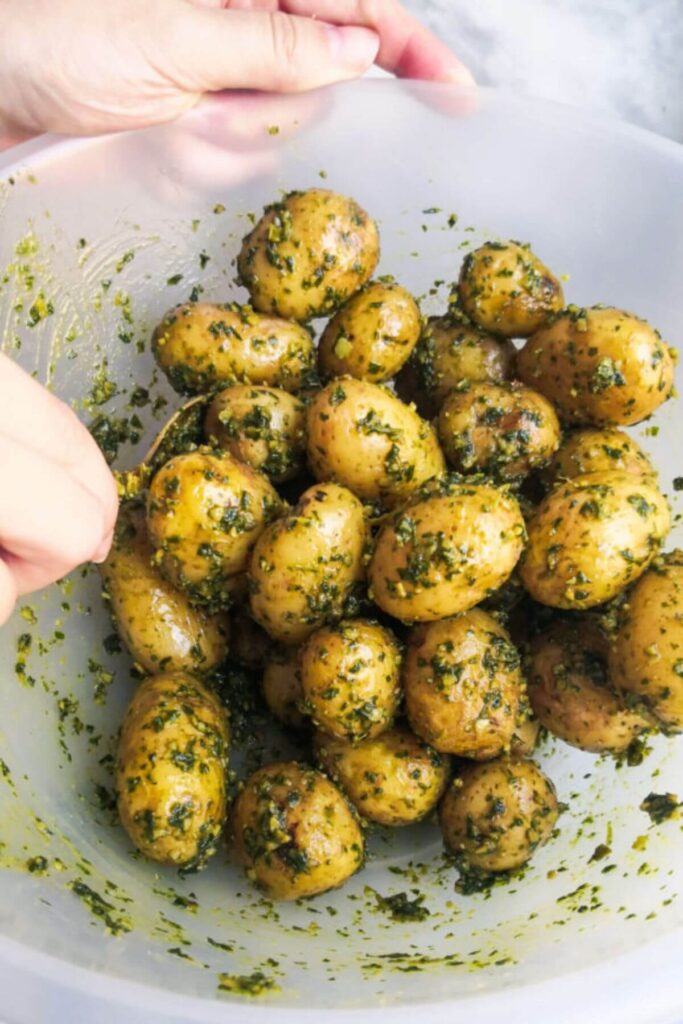 Mixing pesto potatoes in a large clear mixing bowl with a gold spoon.