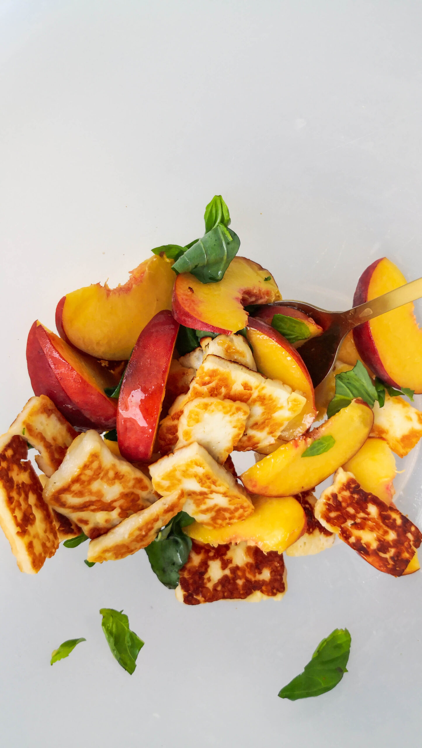 Peach and halloumi salad being mixed in a large clear bowl.