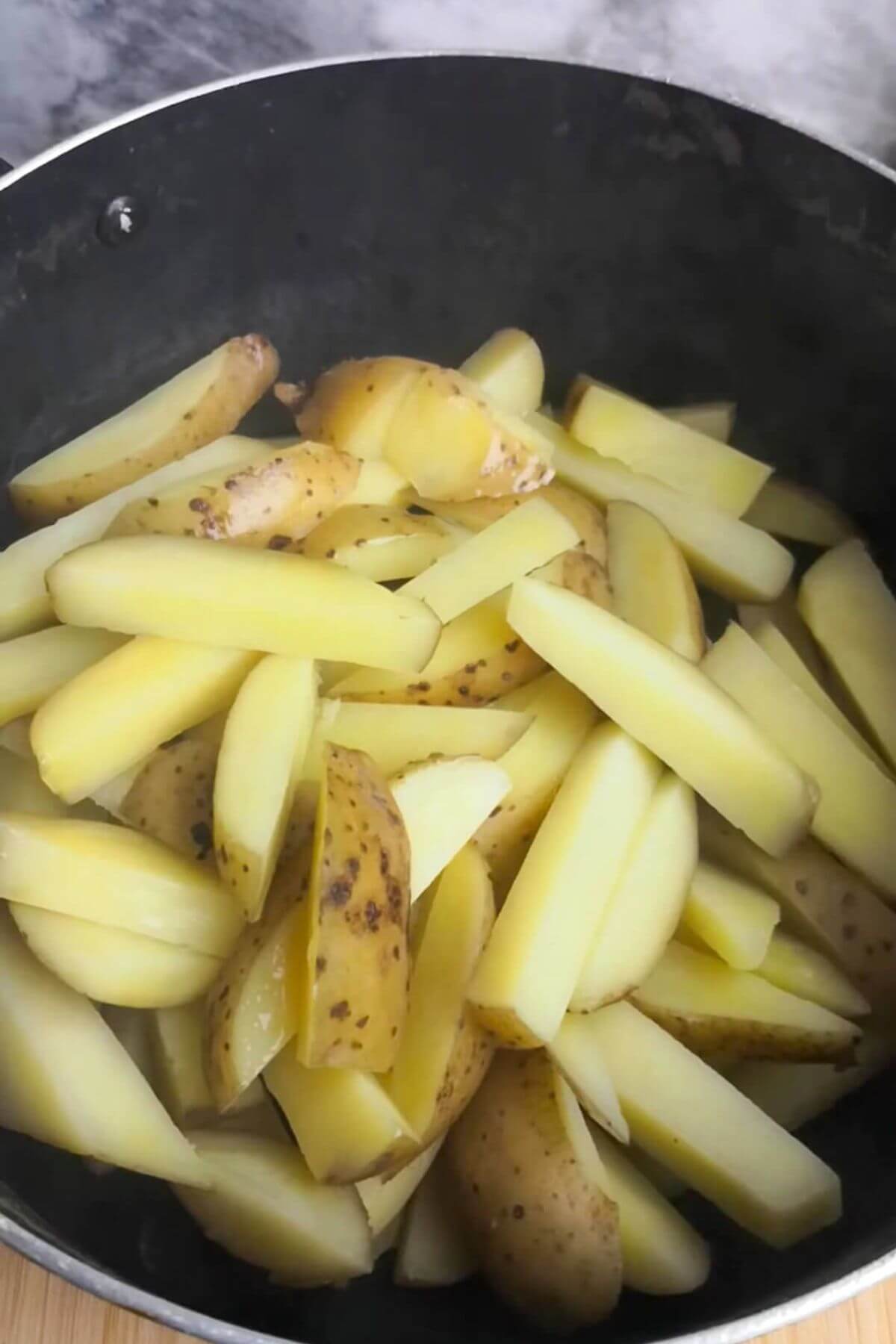 Chips after being par-boiled in a large black pot.