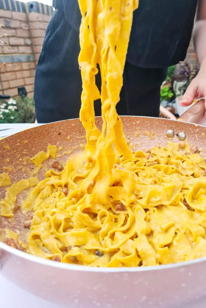 Fettucine being held up out of pink pan by tongs.