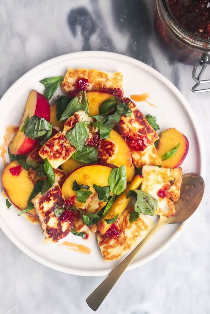 Peach and halloumi salad on a white serving plate with a small gold spoon with a jar of chilli jam in the background.