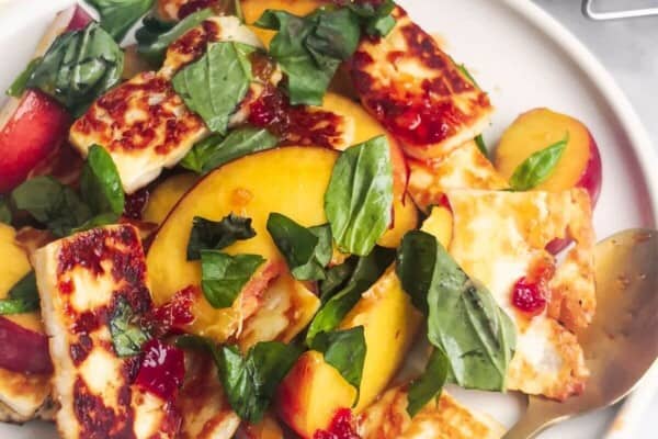 Peach and halloumi salad on a white serving plate with a small gold spoon with a jar of chilli jam in the background.