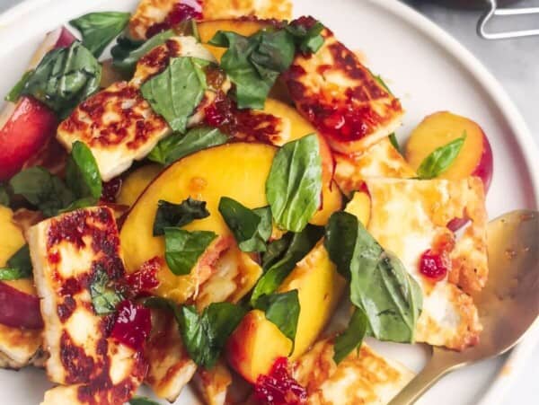 Peach and halloumi salad on a white serving plate with a small gold spoon with a jar of chilli jam in the background.