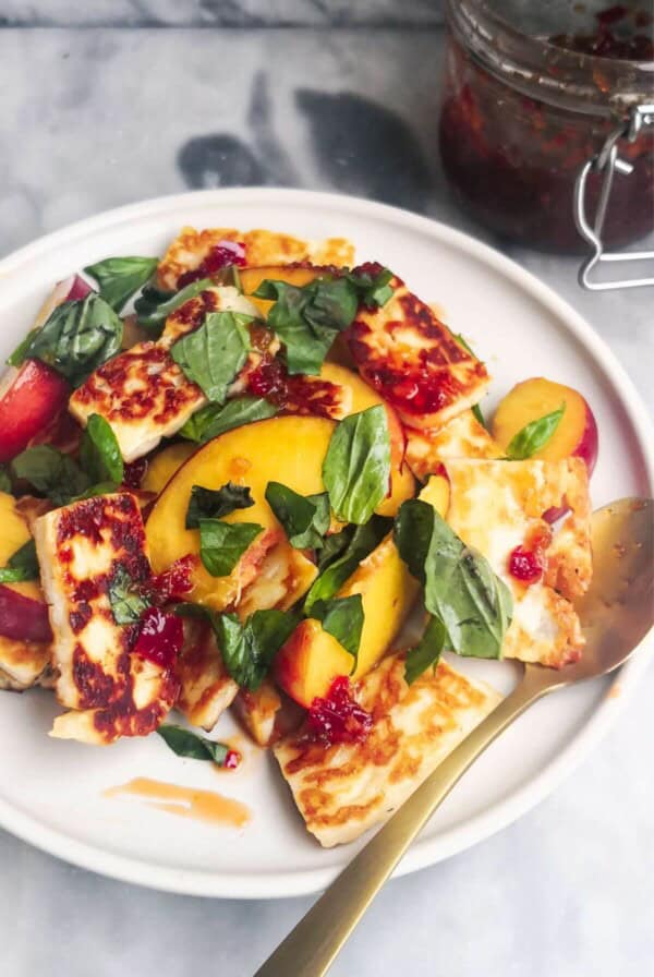 Peach and halloumi salad on a white serving plate with a small gold spoon with a jar of chilli jam in the background.