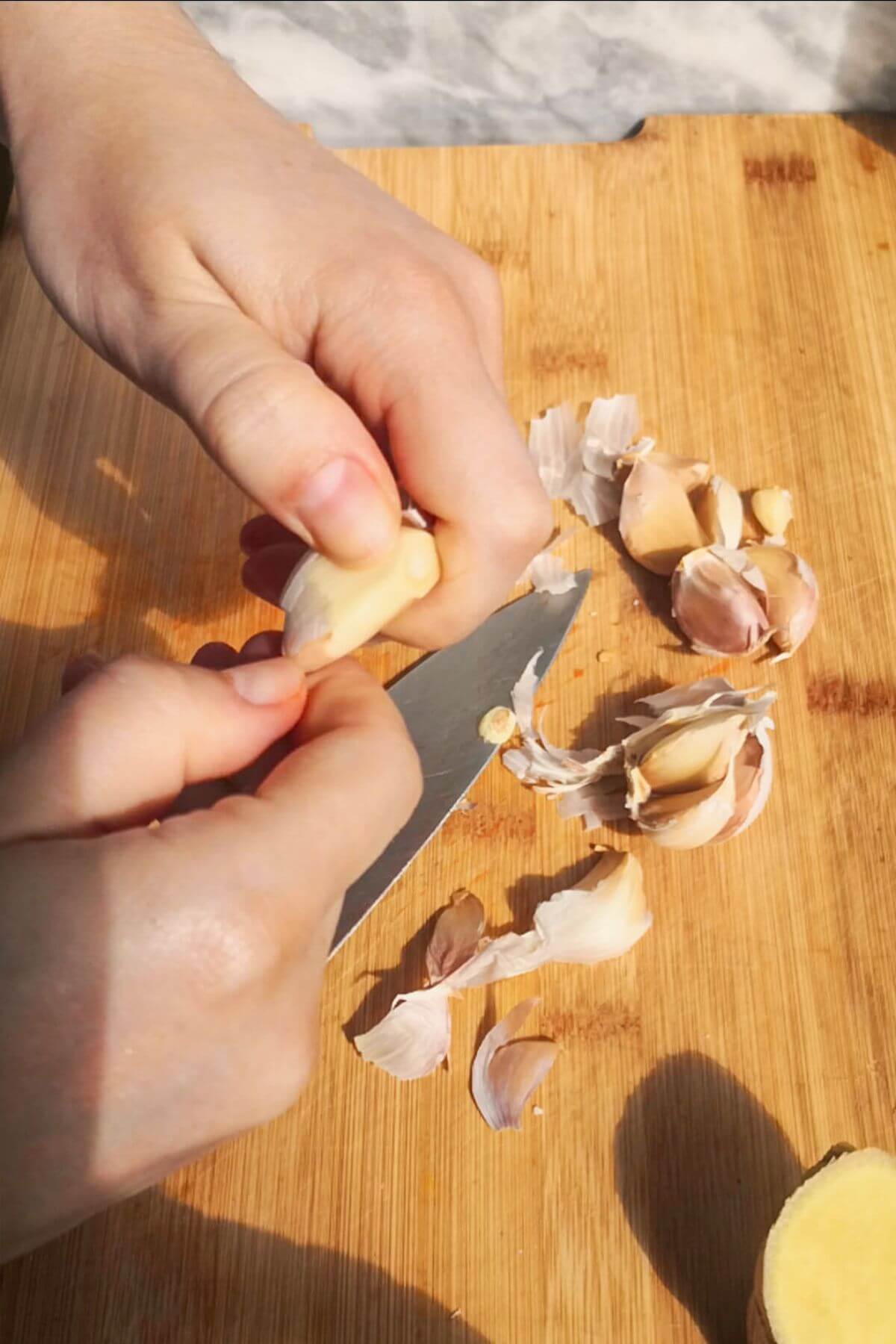 Hand peeling garlic cloves on a wooden board.