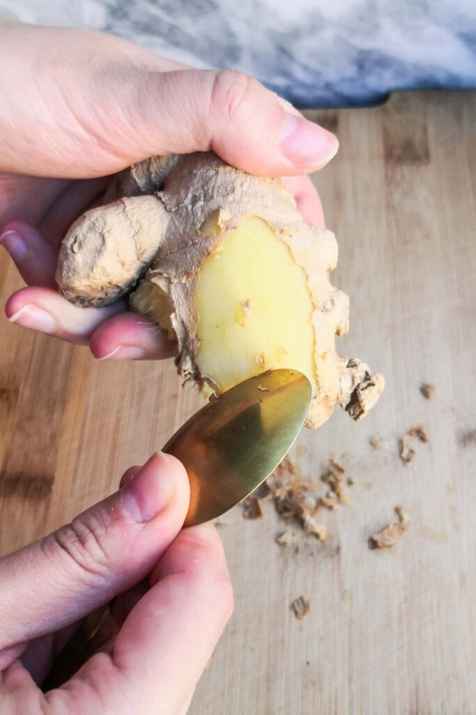 A small gold spoon peeling the skin off fresh ginger.