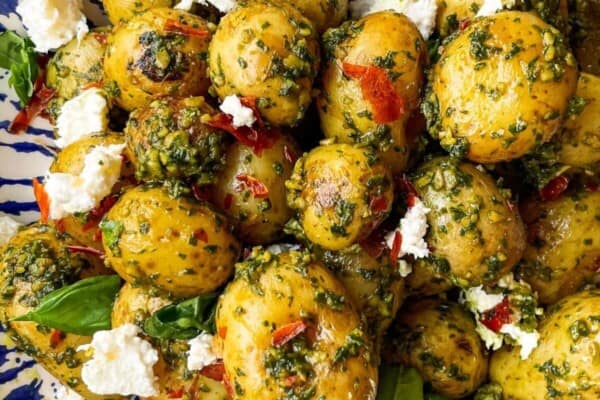 Pesto potatoes with crispy prosciutto and burrata in a blue and white bowl with a gold spoon on a grey marble background.