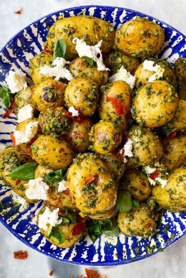 Pesto potatoes with crispy prosciutto and burrata in a blue and white bowl with a gold spoon on a grey marble background.