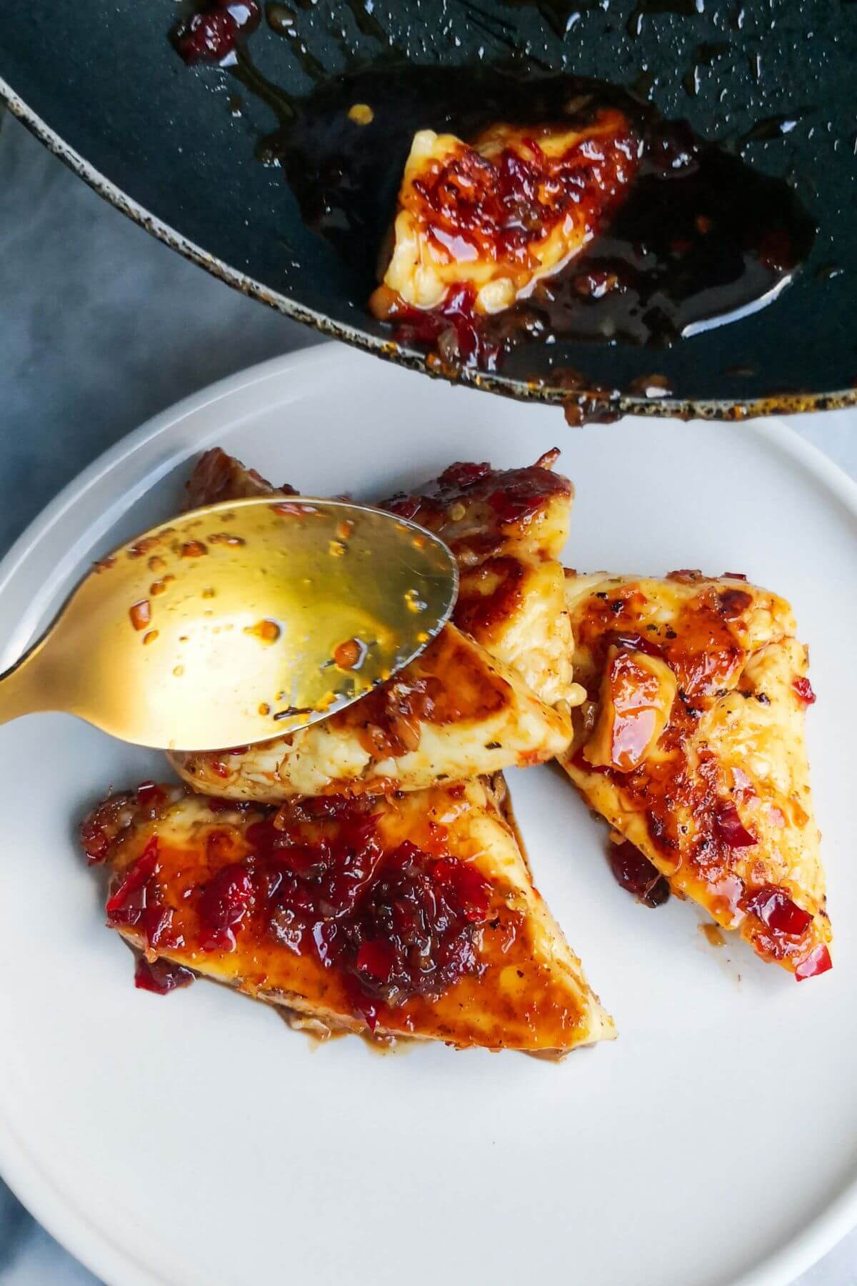 Sweet chilli glazed halloumi triangles being transferred from a small black pan to a white serving plate with a gold spoon.