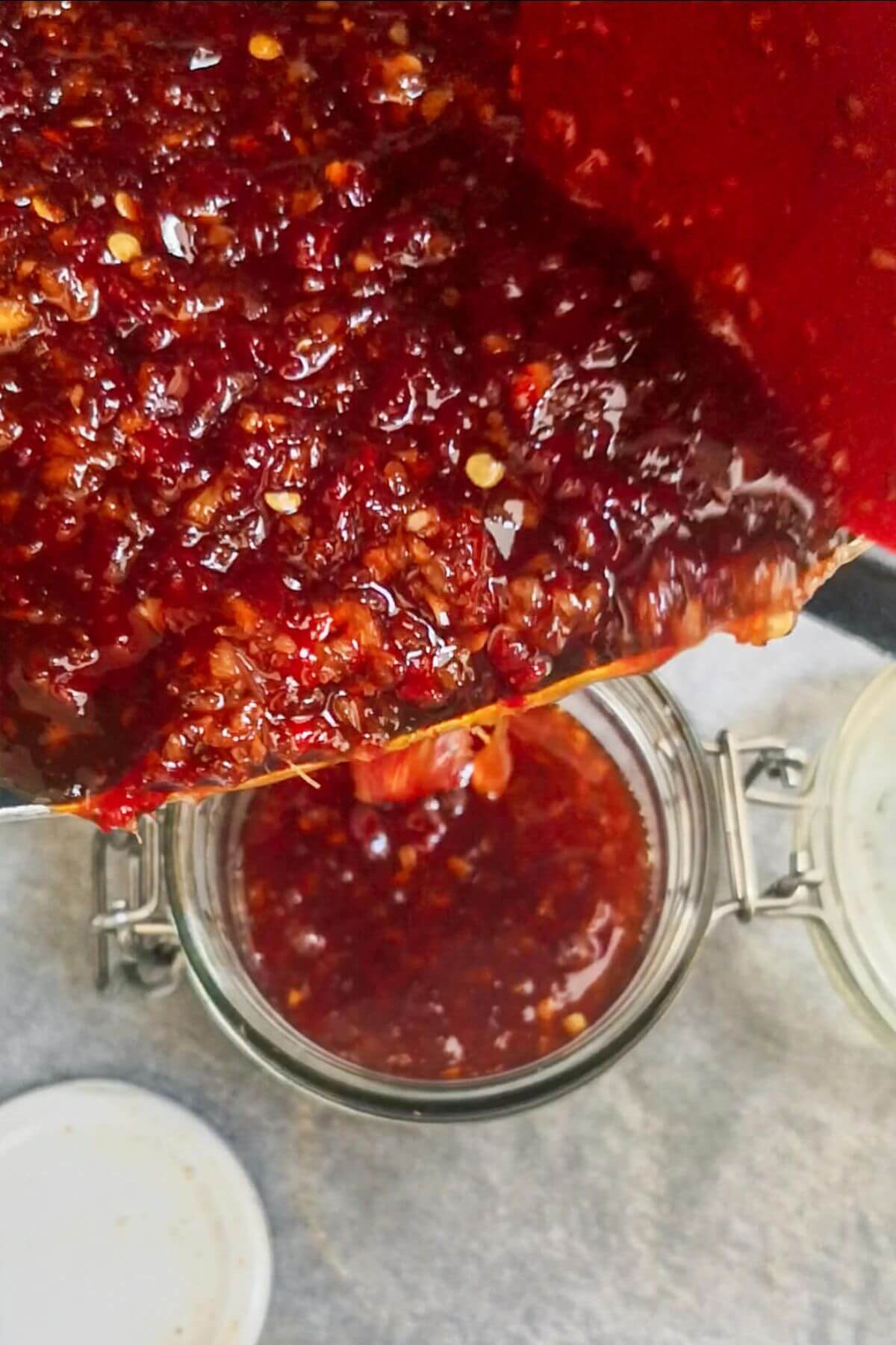 Sticky chilli jam being spooned into a sterilised glass jar.