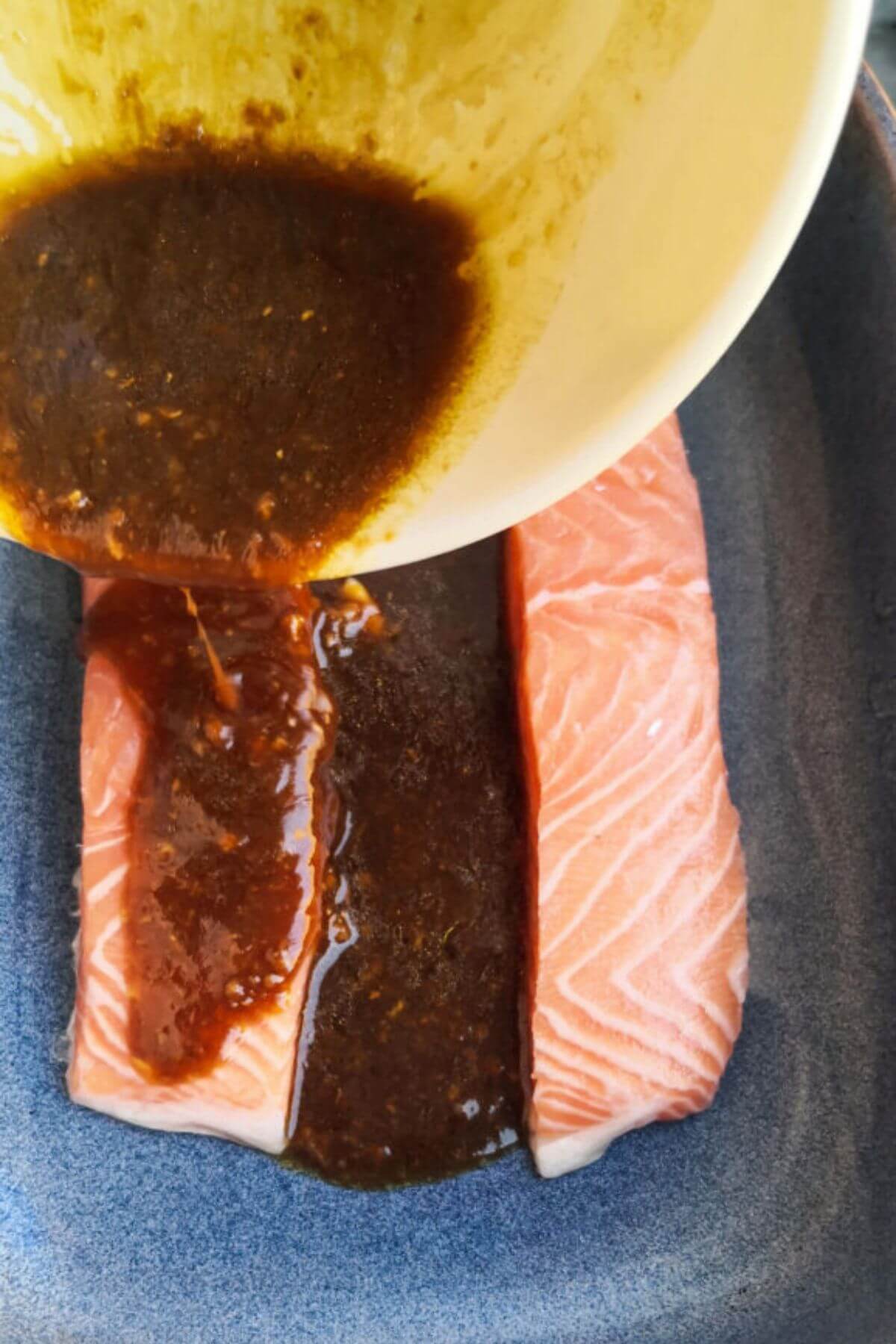 Pouring miso marinade over 2 salmon fillets in a blue oven dish.