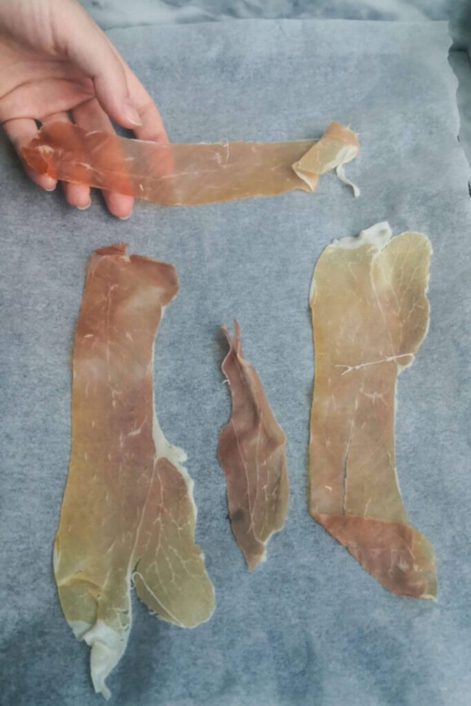Laying out 4 pieces of prosciutto on a baking paper lined oven tray.