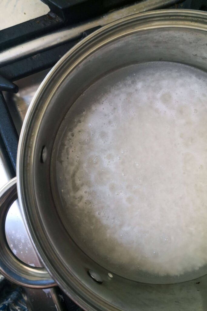 Foamy water appearing on the top of a silver pot filled with sushi rice on the stove top.