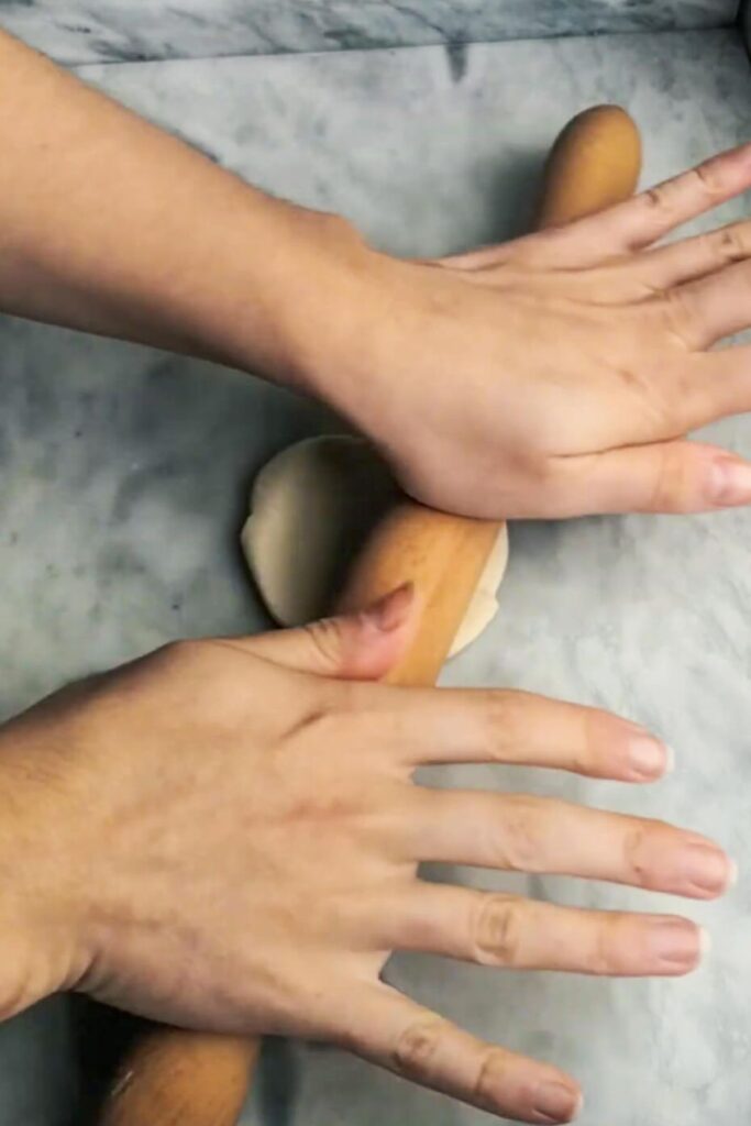 Hands using wooden rolling pin to roll out a small circle of dough.