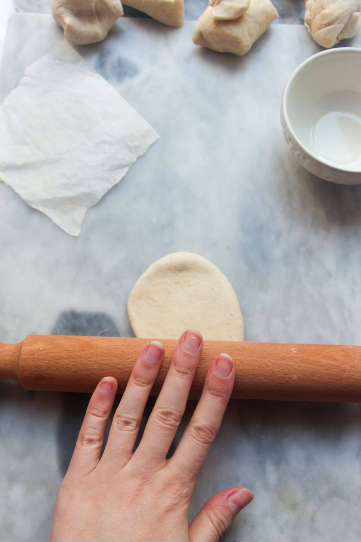 Rolling pin rolling bao bun dough into a longer oval.