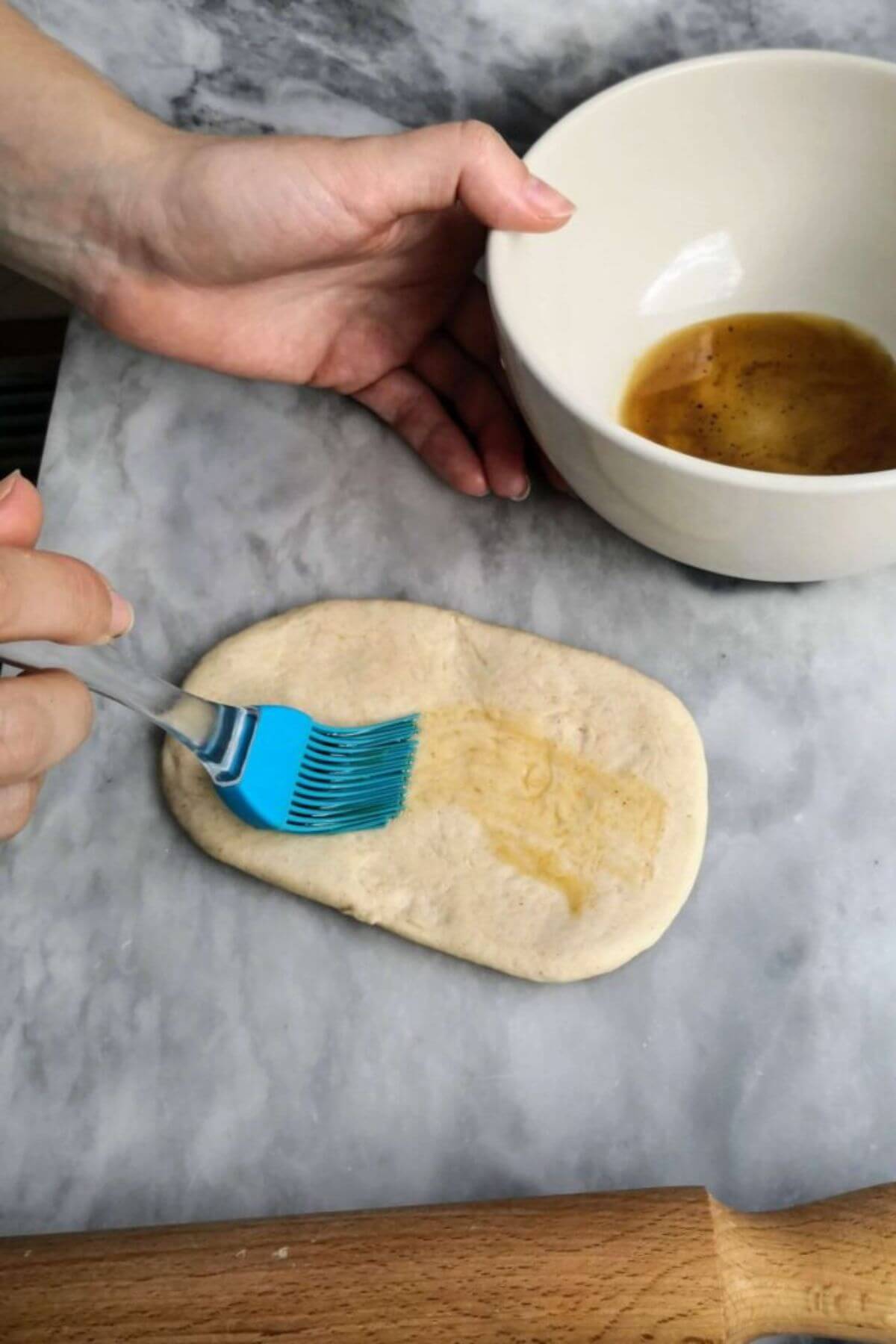 Sesame oil being brushed onto one side of bao bun dough with a blue pastry brush.