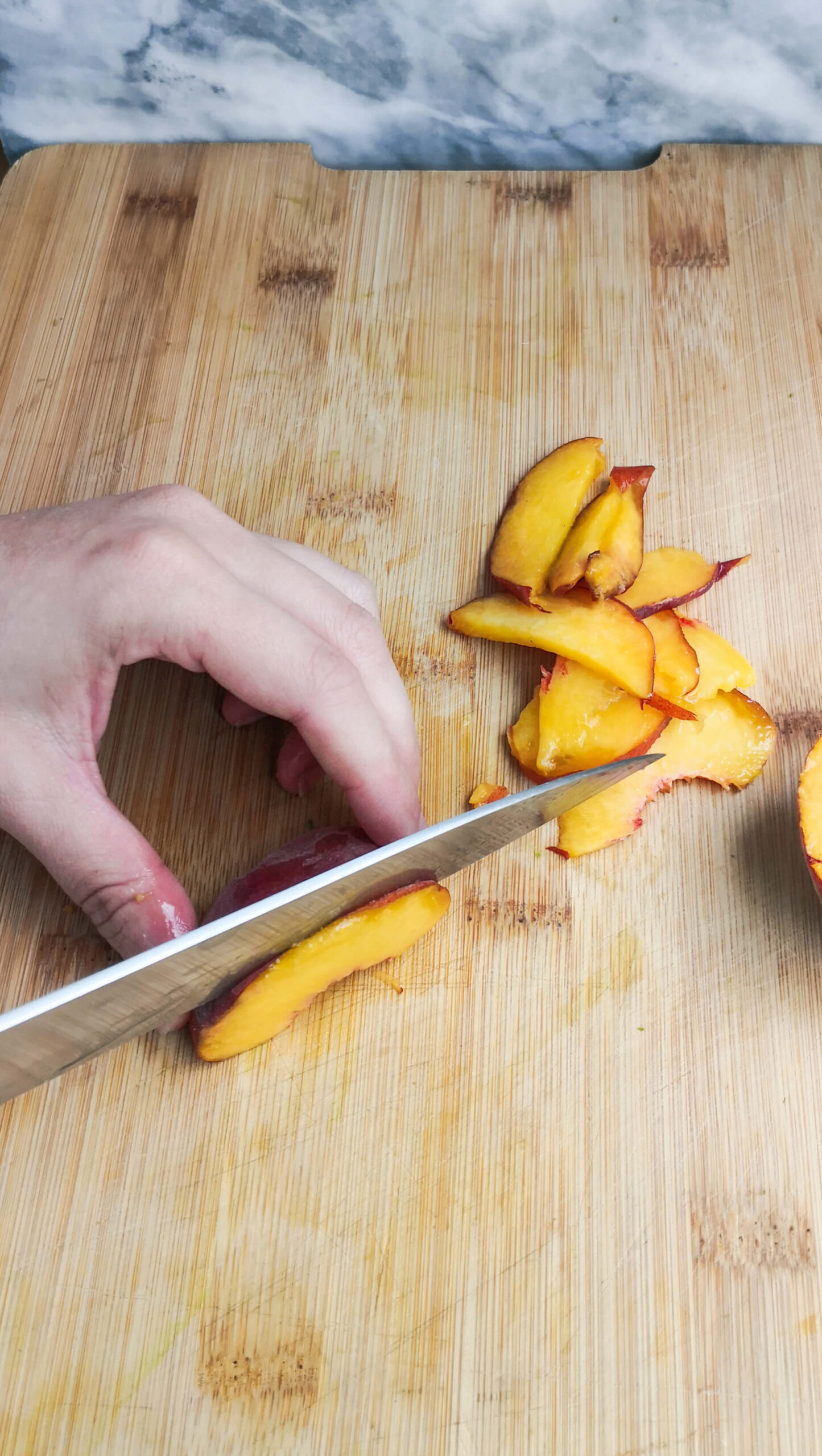 Slicing a peach thinly with a large knife on a wooden board.
