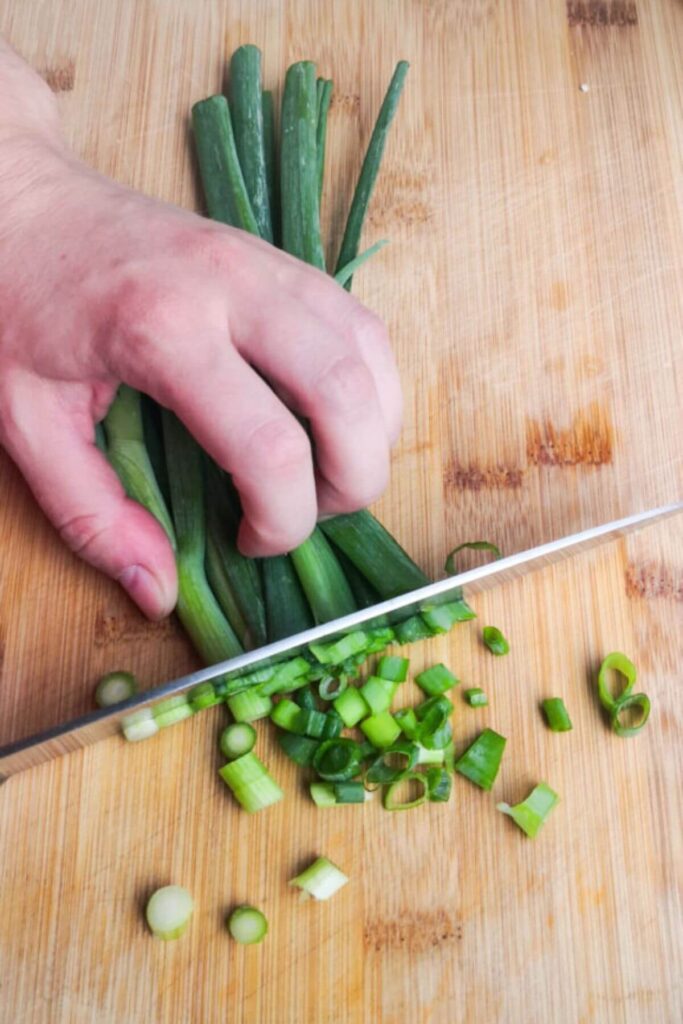 Dicing spring onions with a large knife on a wooden board.