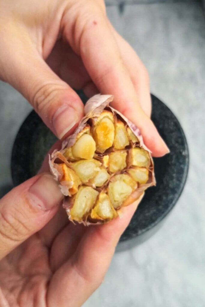 Hands squeezing roasted garlic cloves out of their skin.