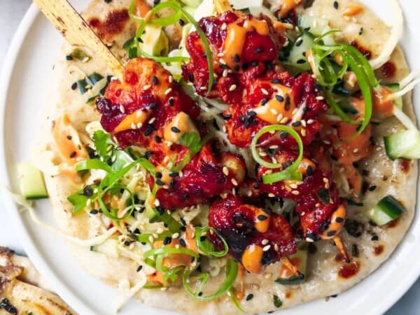 2 gochujang chicken skewers on top of slaw, on a flatbread on a white plate, with flatbreads and gochujang aioli on the side.