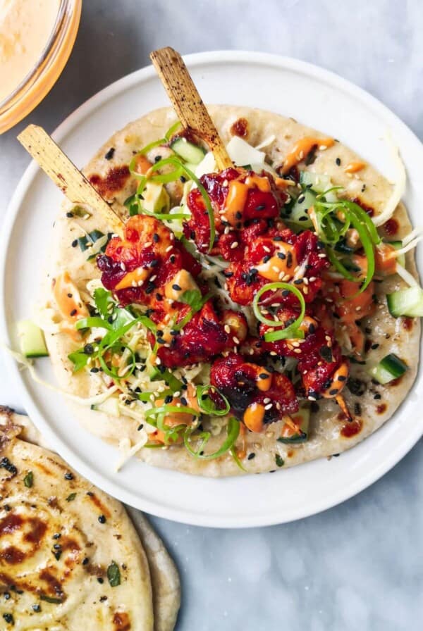 2 gochujang chicken skewers on top of slaw, on a flatbread on a white plate, with flatbreads and gochujang aioli on the side.