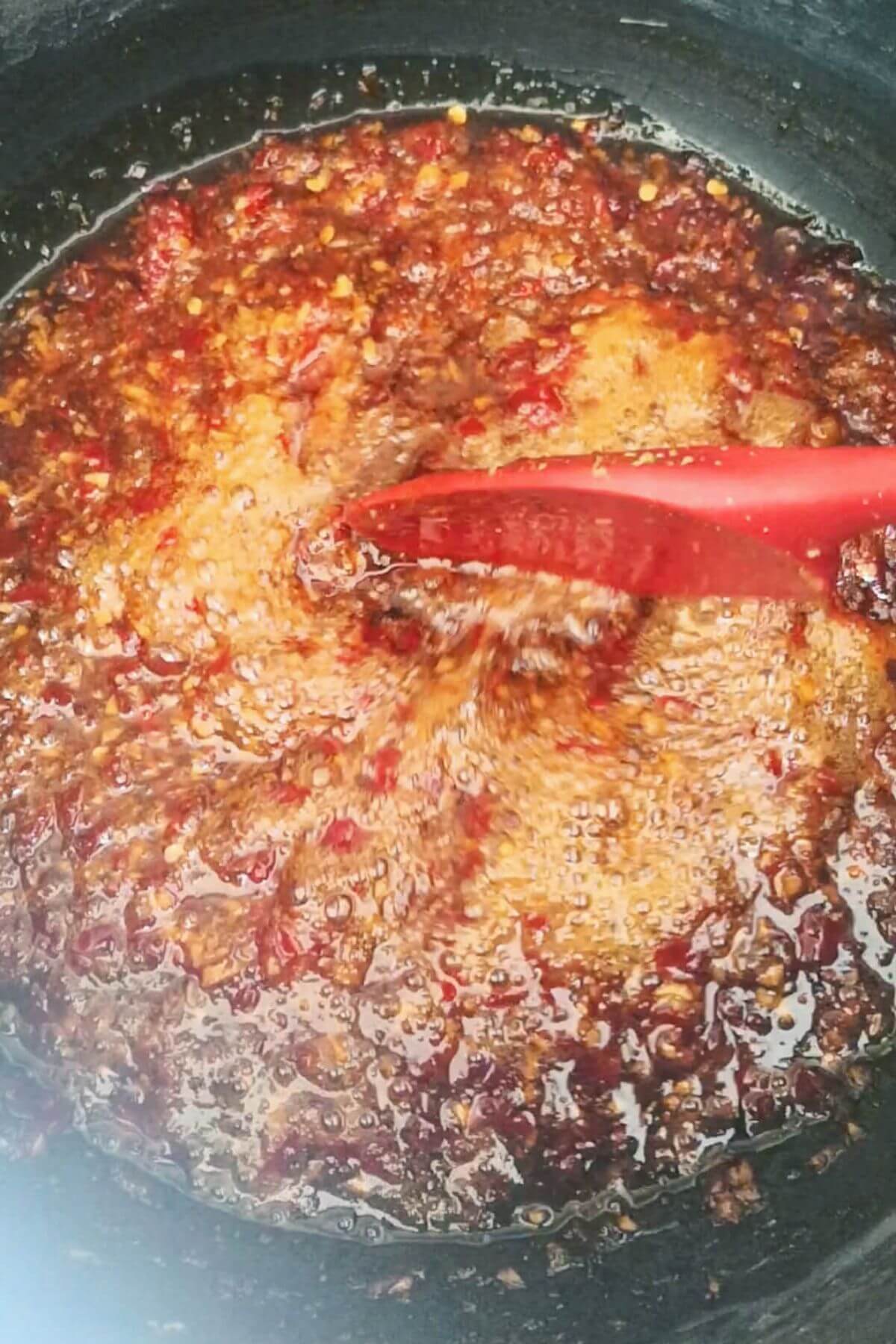 Reduced and bubbling chilli jam being stirred with a red spatula.