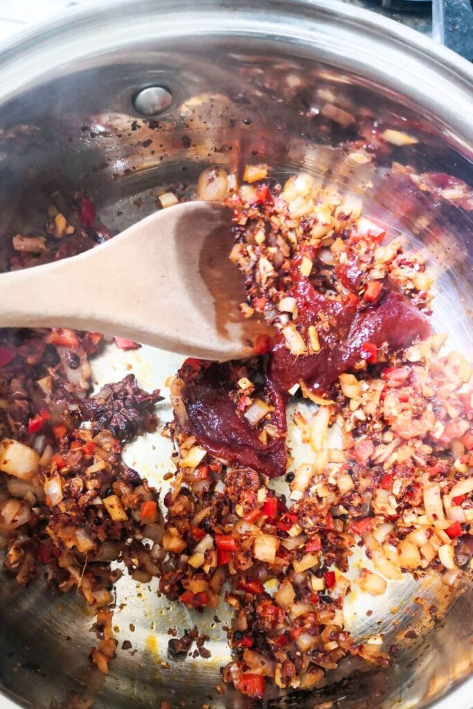 Gochujang paste being stirred into chilli oil ingredients in a small silver pot.