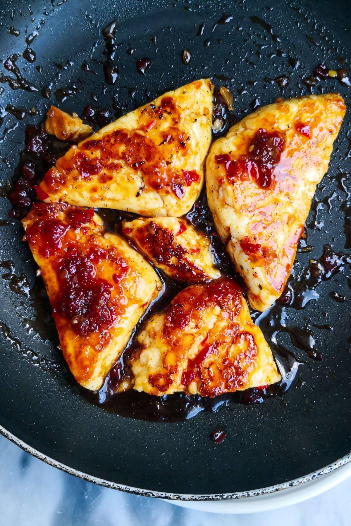 5 golden sweet chilli jam glazed halloumi triangles in a small black pan.