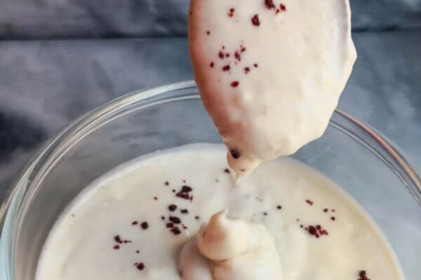 Tahini yogurt sauce being poured off a small gold spoon into a small glass bowl on a grey marble background.