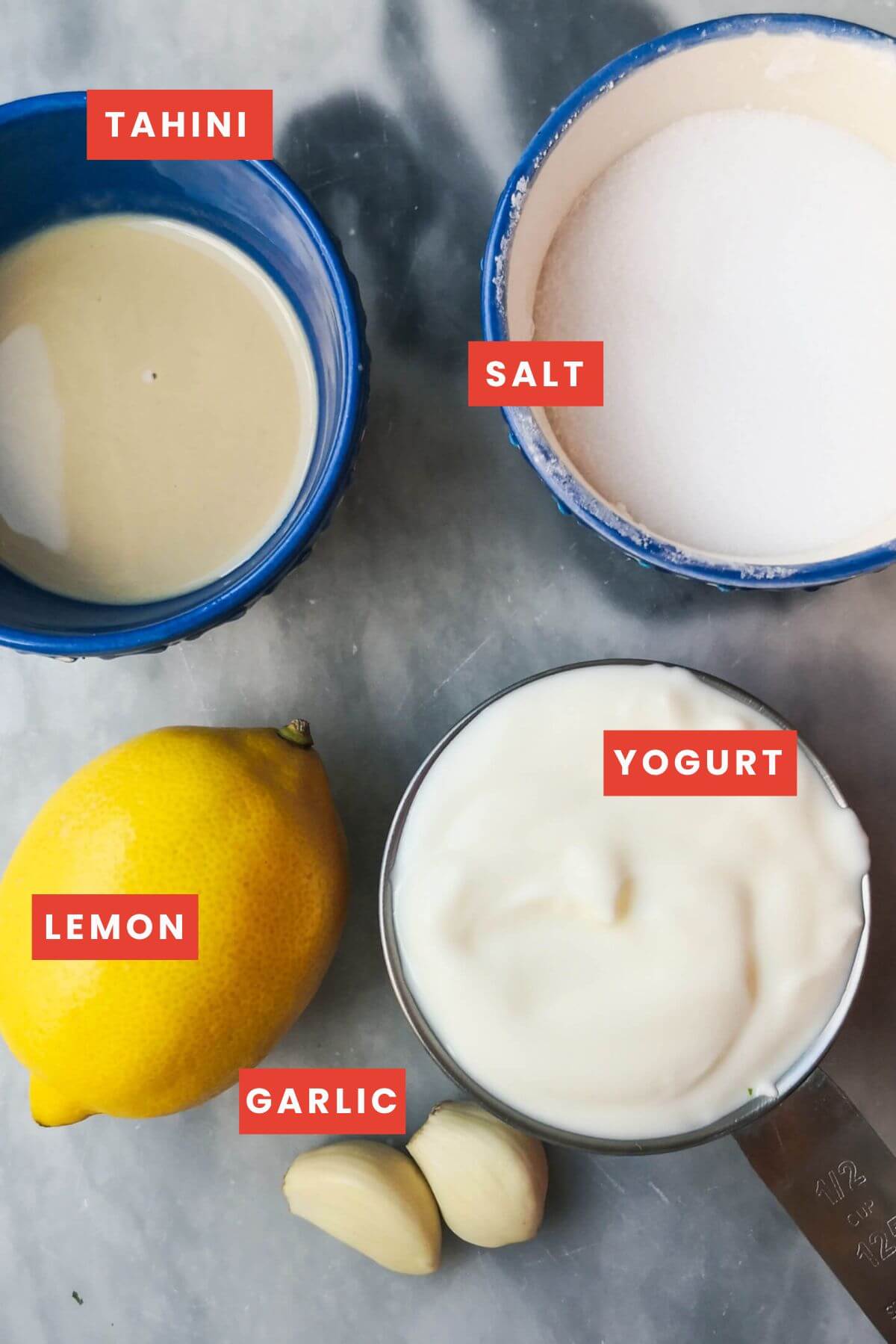 Ingredients for tahini yogurt sauce laid out on a grey marble background.