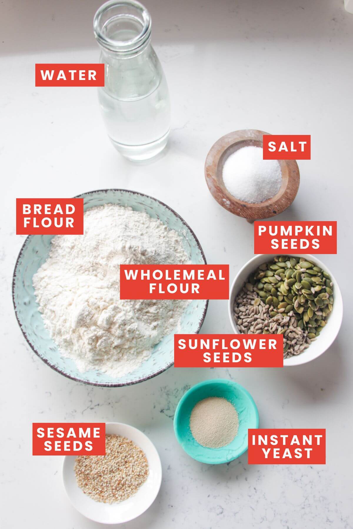 Ingredients for Vogel's style bread laid out on a white marble background and labelled.