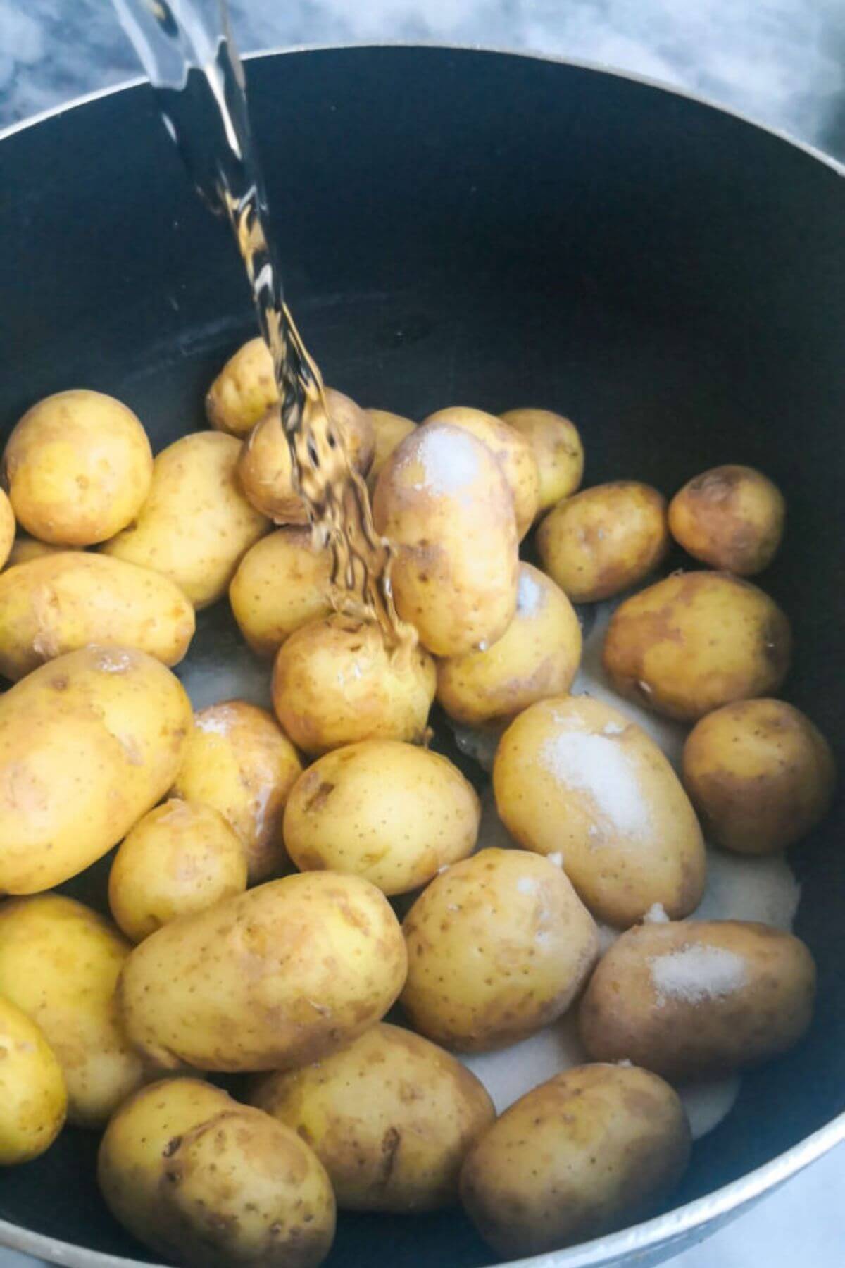 Water being poured into a large black pot filled with baby potatoes.