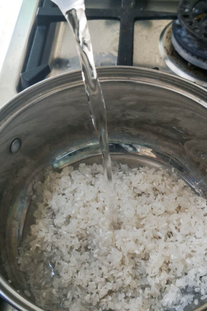 Water being poured into small silver pot with sushi rice in it.