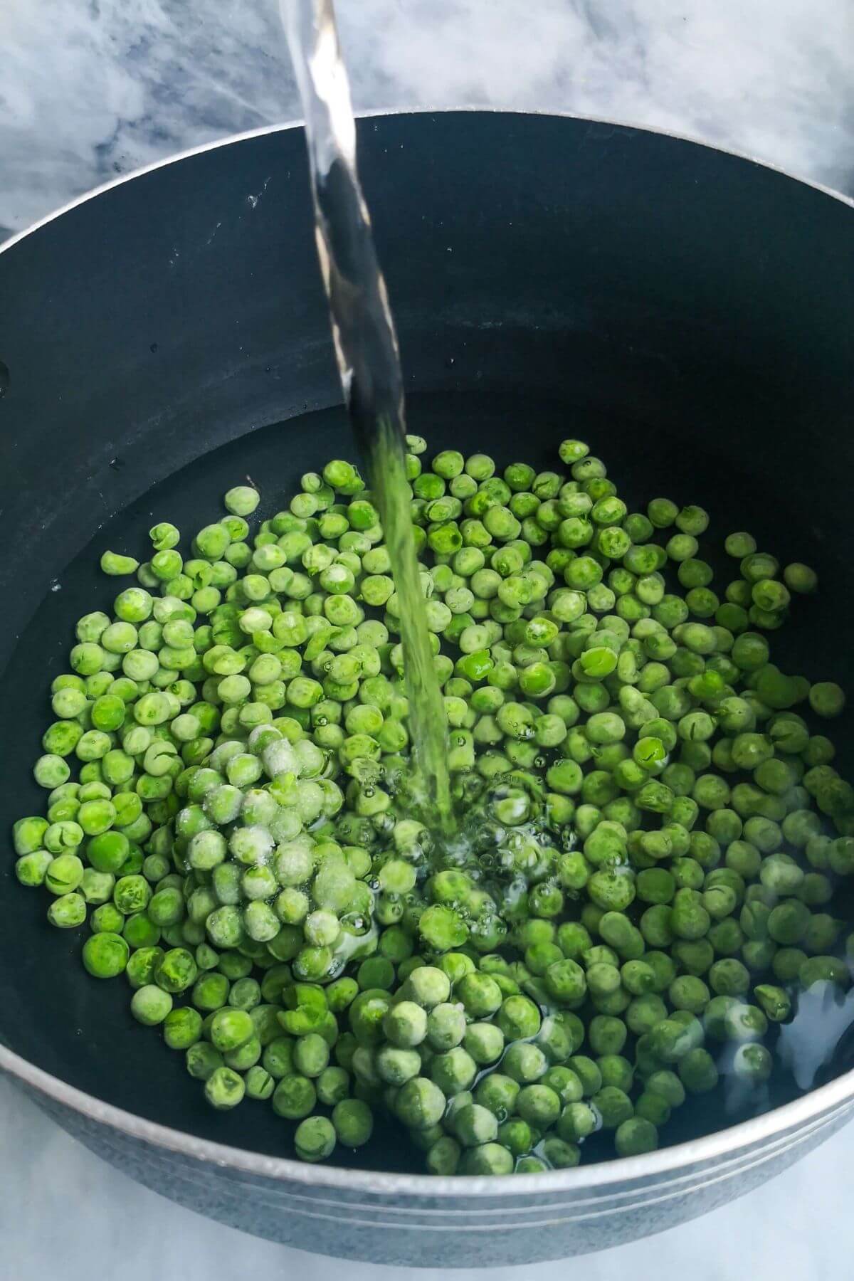 Water being poured into a large black pot filled with peas.