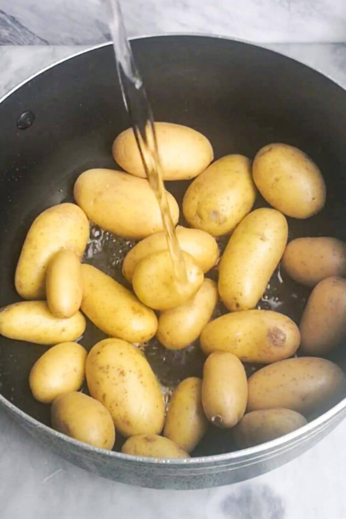 Water being poured into a pot of baby potatoes on a grey marble background.