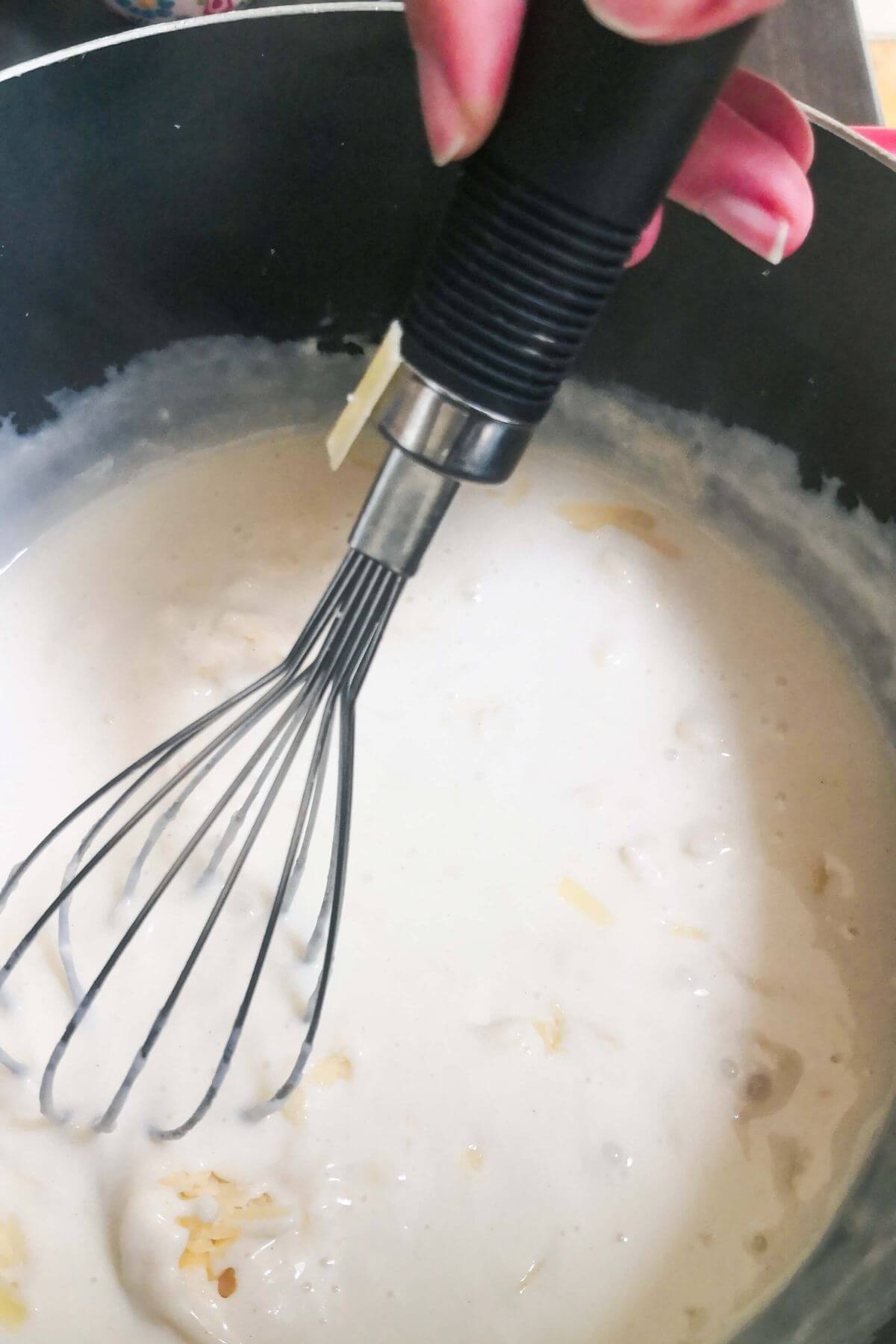 Grated cheese being whisked into the sauce in a large black pot.