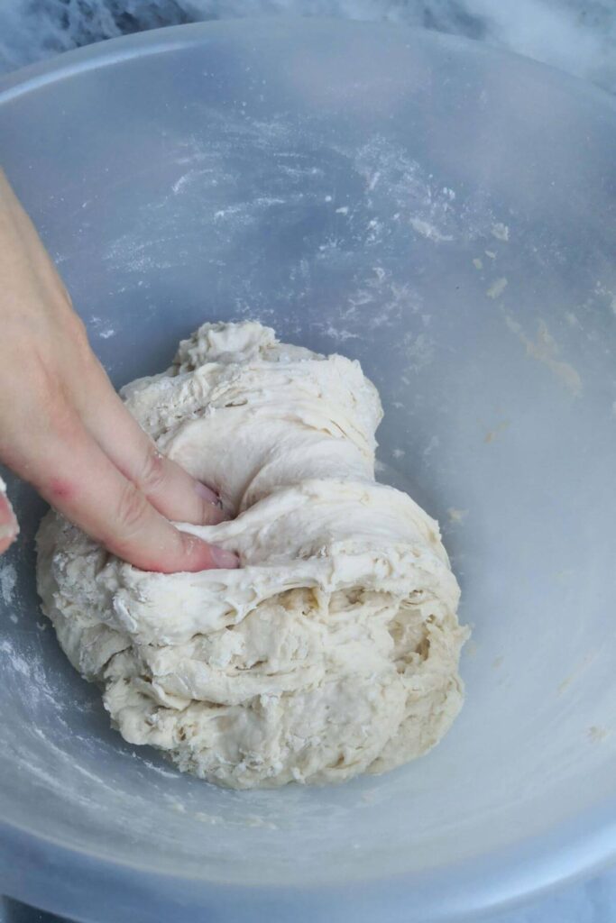Hand folding down dough in a clear mixing bowl.