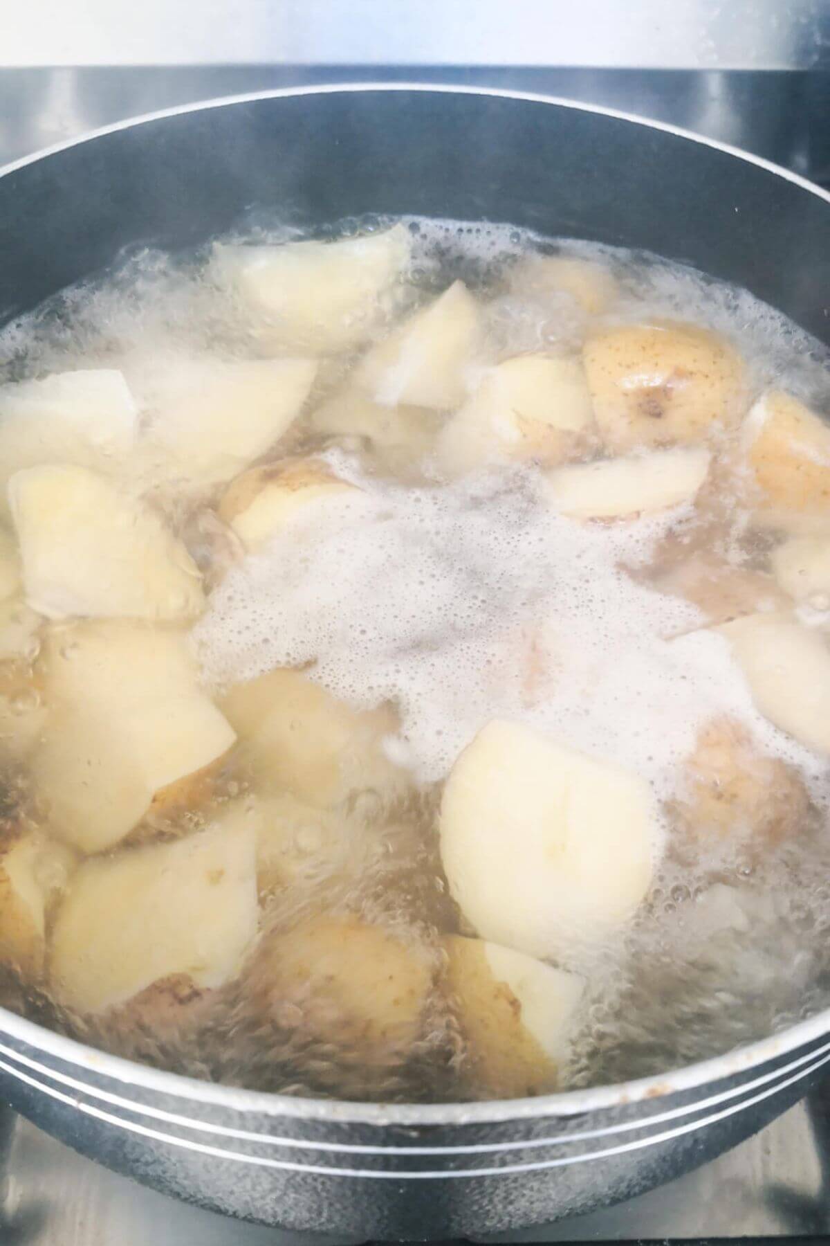 Chopped potatoes boiling in a large pot full of water.