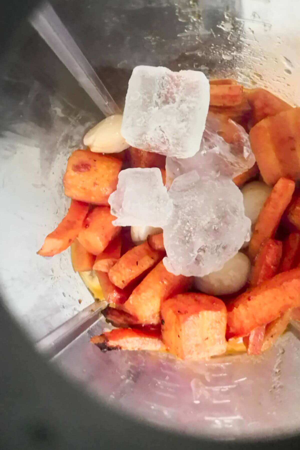 Carrots, butter beans and ice cubes in the bowl of a blender.