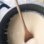 Cheesy bechamel sauce in a pot with a wooden spoon.