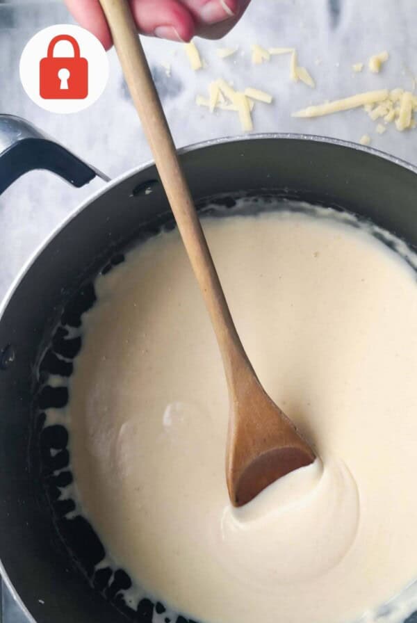 Cheesy bechamel sauce in a pot with a wooden spoon.